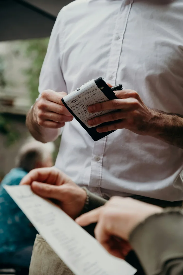 Server writing on a notepad while a guest holds a menu