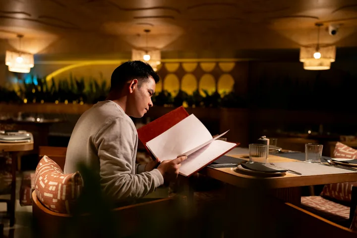 Guest reading a paper menu at a restaurant table