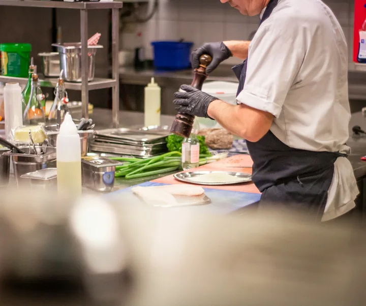 Cook seasoning plates at a station in a busy restaurant kitchen