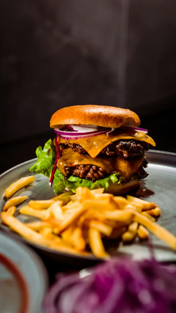 Double cheeseburger with lettuce and red onion beside a pile of fries