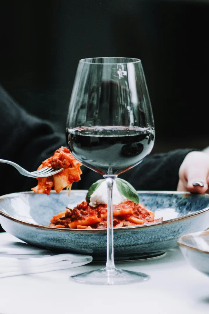 Pasta in tomato sauce topped with mozzarella and basil, beside a glass of red wine