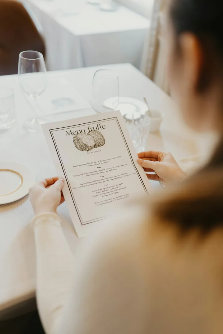 Guest reading a printed dinner menu at a table set with glasses