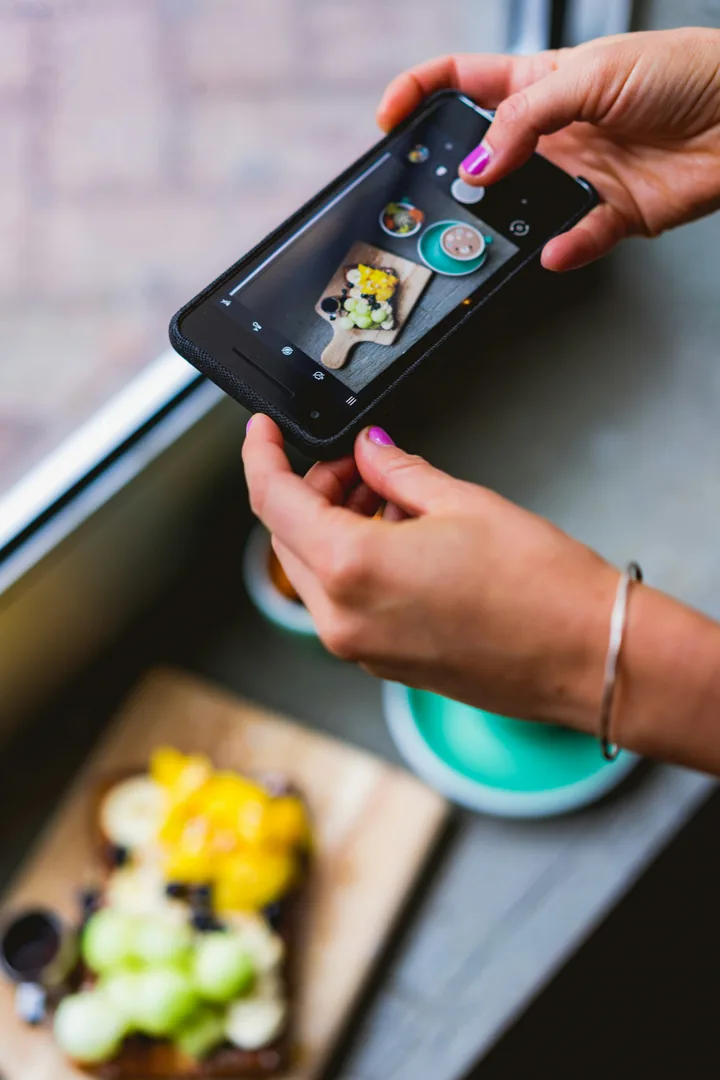 Person using a phone to photograph food beside a window