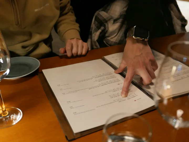 Guest pointing at a dish on a printed menu at a restaurant table