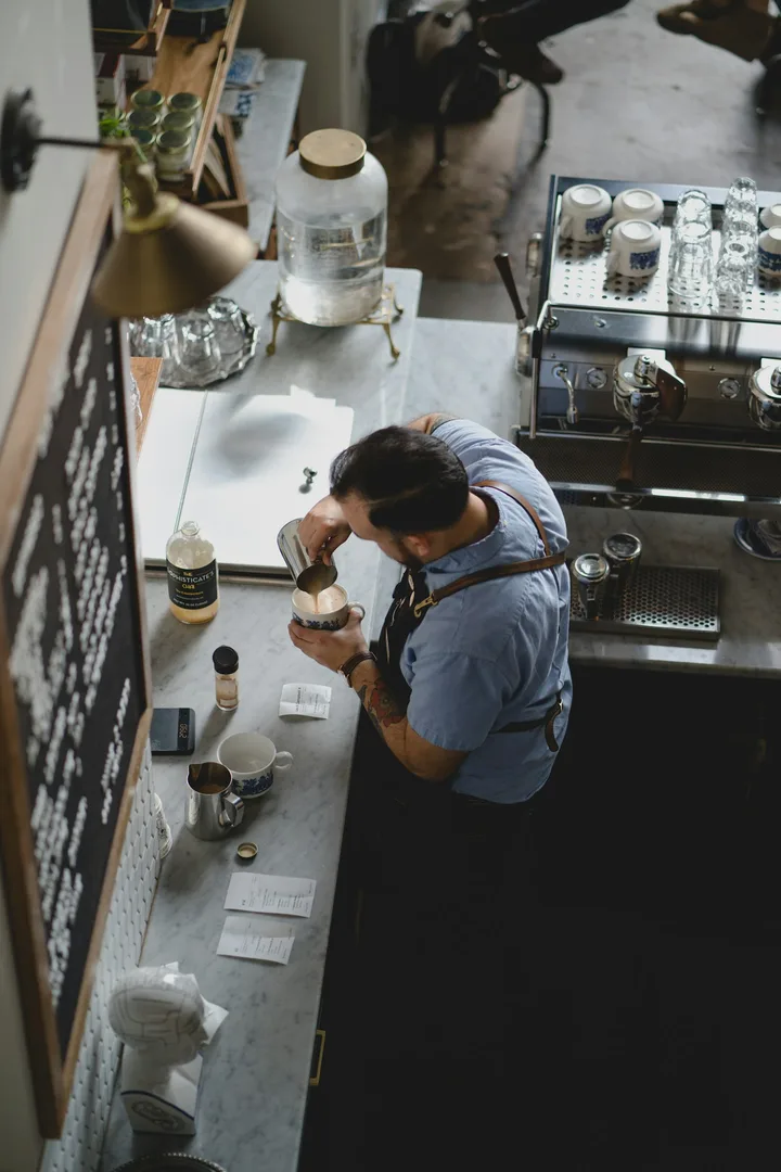 Barista making coffee at a café counter beside a chalkboard menu, seen from above