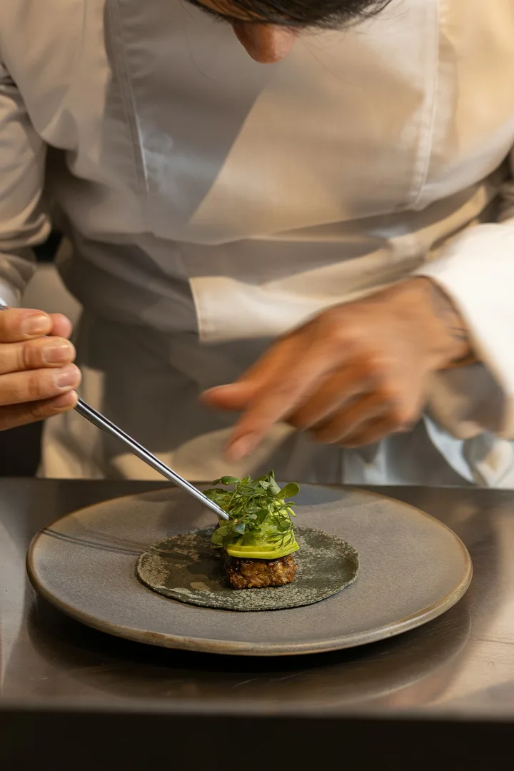 Chef using tweezers to place greens on a small plated course